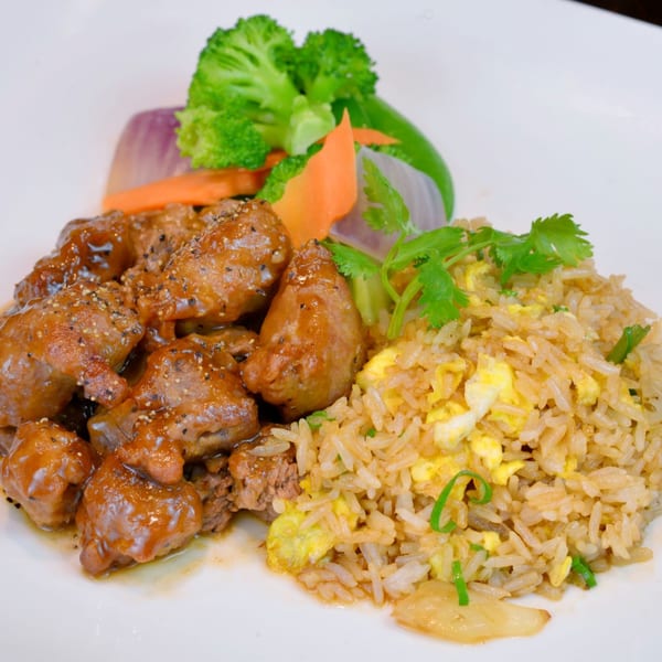Peppered steak cubes with fried rice, broccoli, carrots, and onions on a white plate.