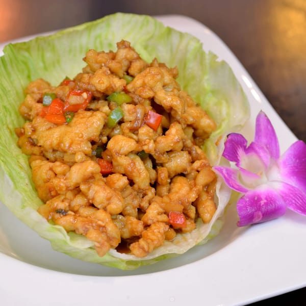Crispy chicken lettuce wraps with red and green peppers, garnished with a purple orchid.