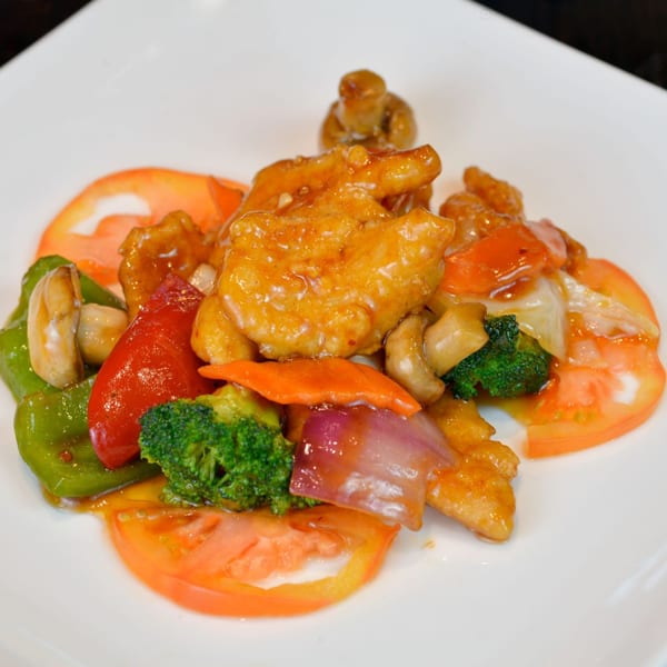 Sweet and sour chicken with broccoli, bell peppers, onions, and mushrooms on a white plate.